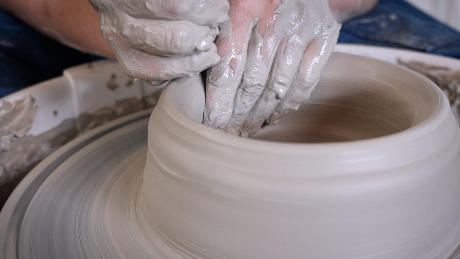 Clay-covered hands shaping the wall of a bowl on a spinning potter's wheel